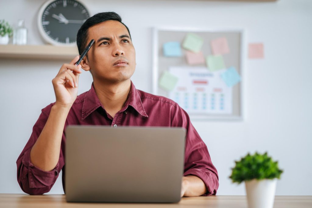 Man thinking while working on laptop at desk
